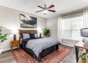 Thumbnail 11 of 23 - Dog-Friendly Apartments in North Austin, TX - Sycamore Springs - Furnished Bedroom with a Ceiling Fan, a Large Window, and Faux Plank Flooring