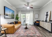 Thumbnail 7 of 23 - Pet-Friendly Apartments in North Austin, TX - Sycamore Springs - Furnished Living Room with Faux Plank Flooring, a Sliding Glass Door to a Private Patio/Balcony, a Ceiling Fan, and Stylish Decor