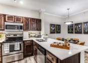 Thumbnail 9 of 23 - 3 Bedroom Apartments in North Austin, TX - Sycamore Springs - Modern Kitchen with Quartz Counters, Wooden Cabinetry, Stainless Steel Appliances, a Dining Area, and Faux Plank Flooring 