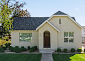 Thumbnail 2 of 6 - A small house with a brown door and windows surrounded by greenery.