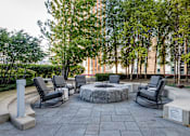 Thumbnail 38 of 42 - A stone fire pit sits in the middle of a patio surrounded by chairs.