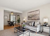 Thumbnail 31 of 46 - A living room with a grey couch, a glass coffee table, and a large abstract painting on the wall.