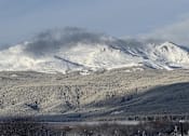 Thumbnail 4 of 8 - A mountain range covered in snow with a cloud of smoke rising from the peak.