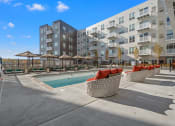 Thumbnail 26 of 57 - a pool with red chairs and umbrellas in front of an apartment building