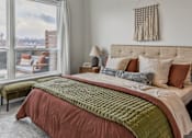 Thumbnail 79 of 83 - A bed with a green comforter and a red blanket is in the foreground of a room with a window showing a view of a snowy landscape.