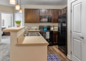 Thumbnail 5 of 22 - Westerville, OH Apartments for Rent - Kenyon Square - Kitchen with Beige Counters, Custom Cabinetry, Black Appliances, Modern Light Fixtures, and Wood-Style Flooring