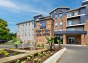 Thumbnail 1 of 22 - Apartments in Westerville, OH with In-Unit Washer and Dryer - Kenyon Square - Apartment Building Exterior with Stone Details, Private Balconies, and Beautiful Landscaping with a Water Fountain
