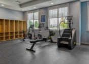 Thumbnail 18 of 79 - a gym with exercise bikes and a chair in a room with windows at The Commons at Rivertown, Grandville, MI