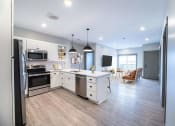 Thumbnail 44 of 79 - a kitchen and living room with white cabinets and stainless steel appliances at The Commons at Rivertown, Grandville, Michigan, 49418