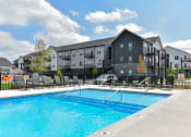 Thumbnail 10 of 79 - a swimming pool with an apartment building in the background at The Commons at Rivertown, Grandville, Michigan