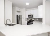 Thumbnail 6 of 19 - A kitchen with white countertops and stainless steel appliances.