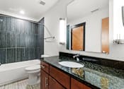 Thumbnail 14 of 21 - A bathroom with a black granite countertop and a white bathtub.