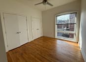 Thumbnail 7 of 10 - A room with a ceiling fan and a window showing a view of a building outside.