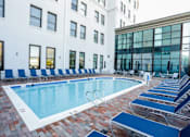 Thumbnail 10 of 21 - A pool surrounded by blue chairs and a white building in the background.