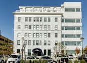 Thumbnail 14 of 21 - A white building with a black awning and cars parked in front.