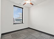 Thumbnail 11 of 21 - A room with a ceiling fan and a window overlooking a cityscape.