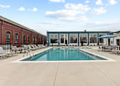 Thumbnail 7 of 17 - A pool surrounded by chairs and a building in the background.