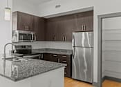 Thumbnail 15 of 17 - A kitchen with a granite countertop and a stainless steel refrigerator.