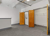 Thumbnail 12 of 17 - A room with a grey carpet and a white wall with a wooden door.