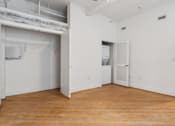 Thumbnail 7 of 10 - A large empty room with wooden floors and white walls.