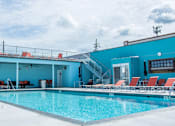 Thumbnail 2 of 10 - A swimming pool with red lounge chairs and a blue building in the background.