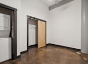 Thumbnail 8 of 13 - A room with a brown floor and a white wall with a door open.