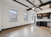 Thumbnail 3 of 13 - A large empty room with a kitchen area on the right side.