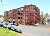 Thumbnail 1 of 5 - A red brick building with a black car in front of it.