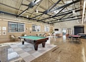 Thumbnail 6 of 22 - A pool table is in the middle of a room with a high ceiling and lots of windows.