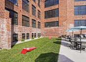 Thumbnail 4 of 22 - A red blanket is on the grass in front of a brick building.
