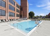 Thumbnail 2 of 22 - A swimming pool on a rooftop with lounge chairs and a building in the background.