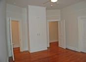 Thumbnail 19 of 22 - A room with white walls and wooden floors has a ceiling fan and three white doors.