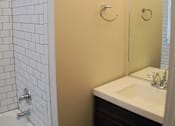 Thumbnail 18 of 22 - A white tiled shower next to a sink in a bathroom.