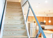 Thumbnail 15 of 22 - A staircase with a metal railing leads to a kitchen area.