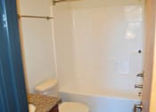 Thumbnail 5 of 6 - A white toilet sits next to a white bathtub in a bathroom.
