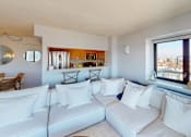 Thumbnail 11 of 43 - A white couch with pillows sits in a living room with a view of the city at 10 West Apartments, New York 11561