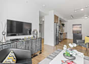 Thumbnail 6 of 39 - a living room with a large tv and a kitchen in the background at 8000 Uptown Apartments, Broomfield, CO