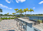 Thumbnail 35 of 46 - a patio with a bar and chairs and a lake in the background at Artesia at Lakewood Ranch Apartments, Bradenton, Florida