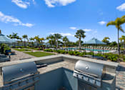 Thumbnail 36 of 46 - two bbqs on a patio overlooking a pool with palm trees at Artesia at Lakewood Ranch Apartments, Florida 34211