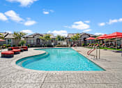Thumbnail 31 of 37 - a swimming pool with red chairs and umbrellas and apartments in the background at Soleil at Canyon Trails Apartments, Goodyear, AZ, 85338