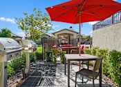 Thumbnail 35 of 37 - a patio with an umbrella and a table with chairs and a grill at Soleil at Canyon Trails Apartments, Goodyear, AZ, 85338