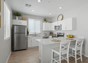 Thumbnail 3 of 43 - a kitchen with white cabinets and a white island with two stools at Sienna at South Mountain Apartments, Laveen, AZ