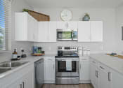Thumbnail 16 of 43 - a kitchen with white cabinets and stainless steel appliances and a clock at Sienna at South Mountain Apartments, Laveen, AZ, 85339