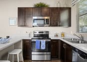 Thumbnail 3 of 33 - a kitchen with stainless steel appliances and dark wood cabinets at Olive Queen Creek Apartments, Queen Creek, 85142