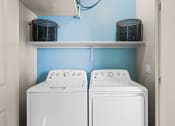 Thumbnail 16 of 33 - the washer and dryer in the laundry room of a house with blue walls at Olive Queen Creek Apartments, Queen Creek, AZ