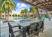 Thumbnail 54 of 65 - A wooden table and chairs are set up under a pergola by a pool. at Centre Pointe Apartments, Melbourne, FL, 32940