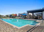 Thumbnail 23 of 33 - a resort style pool with lounge chairs and umbrellas next to a building at Olive Queen Creek Apartments, Queen Creek, AZ, 85142