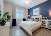 Thumbnail 4 of 15 - A bedroom with a bed, nightstand, and a plant. at Vistoria At Marley Park Apartments, Arizona