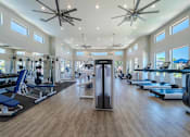 Thumbnail 10 of 15 - A spacious gym with a variety of equipment and a ceiling fan at Vistoria At Marley Park Apartments, Surprise, 85379