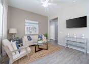 Thumbnail 4 of 15 - A living room with a white couch, a chair, a coffee table, and a flat screen TV mounted on the wall. at Vistoria At Country Place Apartments, Tolleson, AZ, 85353